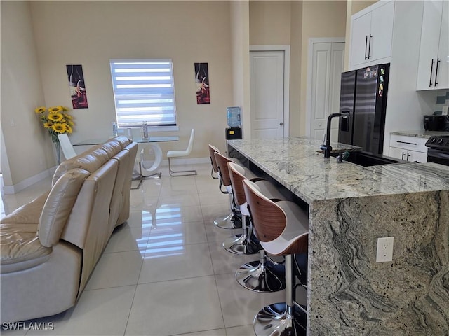 kitchen featuring a breakfast bar area, light tile patterned floors, black refrigerator with ice dispenser, white cabinets, and a sink