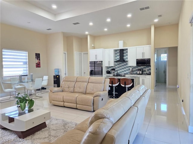 living area with a towering ceiling, light tile patterned floors, visible vents, and recessed lighting