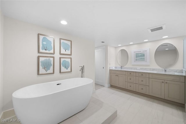 bathroom with visible vents, double vanity, recessed lighting, a freestanding tub, and a sink