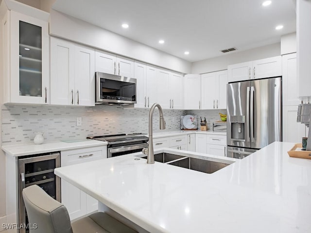 kitchen featuring a sink, stainless steel appliances, light countertops, wine cooler, and glass insert cabinets