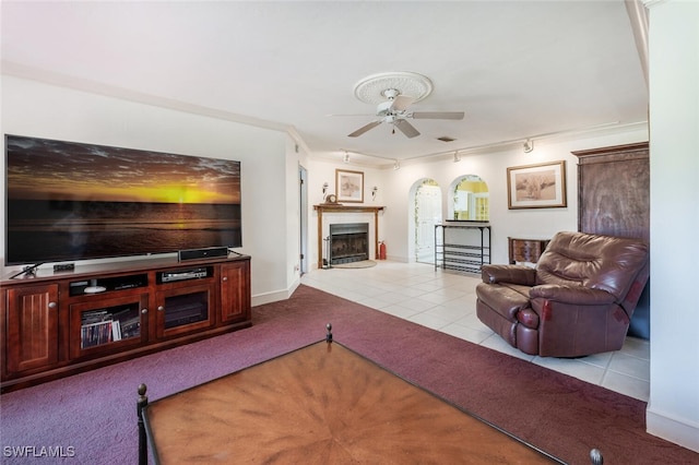 carpeted living room featuring tile patterned flooring, a fireplace with raised hearth, ceiling fan, ornamental molding, and arched walkways