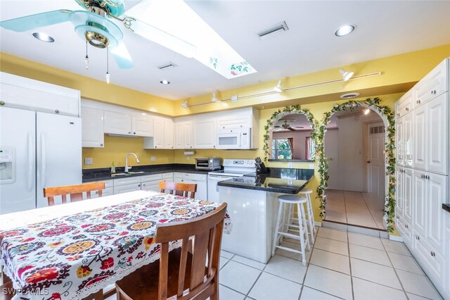 kitchen featuring dark countertops, white appliances, arched walkways, a peninsula, and ceiling fan