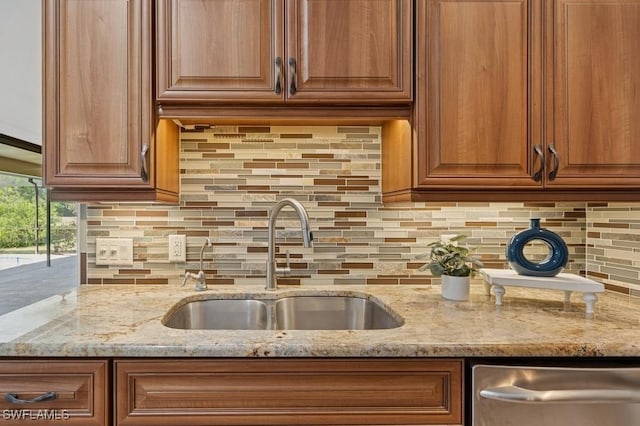 kitchen with brown cabinets, a sink, tasteful backsplash, light stone countertops, and dishwasher