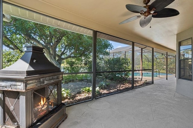 unfurnished sunroom featuring a ceiling fan, a healthy amount of sunlight, and a warm lit fireplace