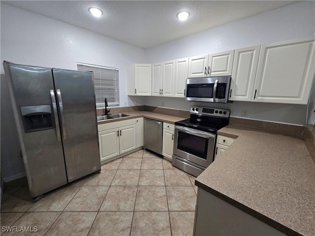 kitchen with light tile patterned floors, appliances with stainless steel finishes, white cabinets, and a sink