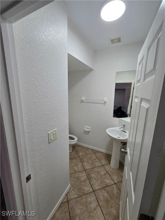 half bath with toilet, a sink, visible vents, baseboards, and tile patterned floors