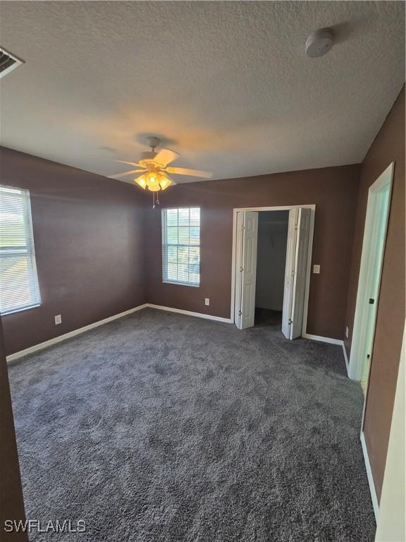 unfurnished bedroom with a textured ceiling, carpet, visible vents, and baseboards