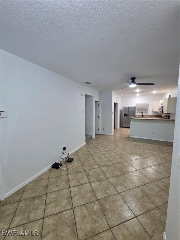 unfurnished living room featuring ceiling fan, a textured ceiling, baseboards, and light tile patterned floors