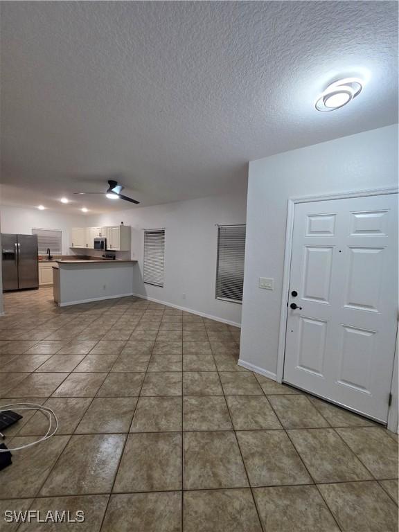 unfurnished living room featuring tile patterned flooring, ceiling fan, a textured ceiling, and baseboards