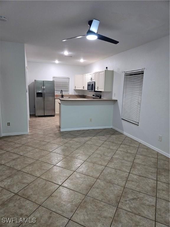 kitchen with appliances with stainless steel finishes, a ceiling fan, white cabinets, a sink, and a peninsula