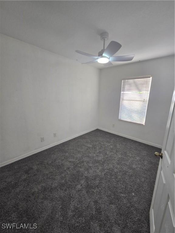 spare room with dark carpet, a ceiling fan, and baseboards