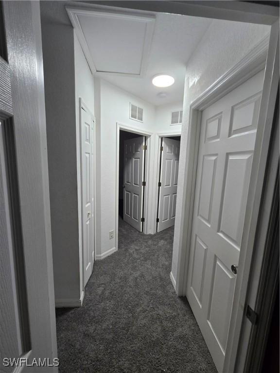 corridor featuring dark carpet, visible vents, and baseboards