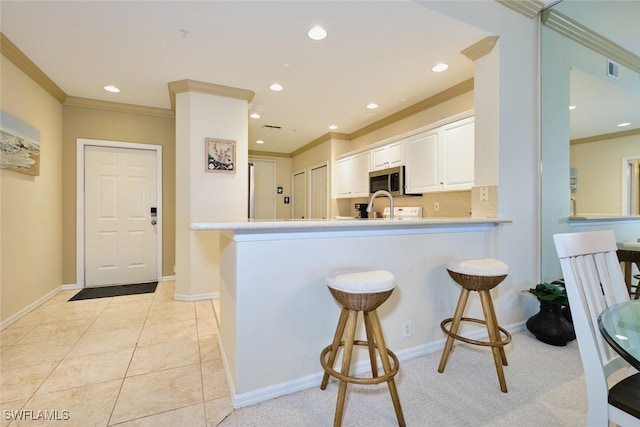 kitchen featuring stainless steel microwave, a breakfast bar, light countertops, crown molding, and white cabinetry