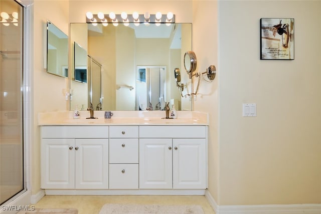 full bathroom with tiled shower, a sink, baseboards, and double vanity