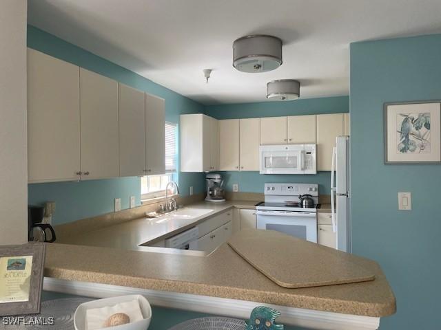 kitchen featuring white appliances, a peninsula, a sink, light countertops, and white cabinets