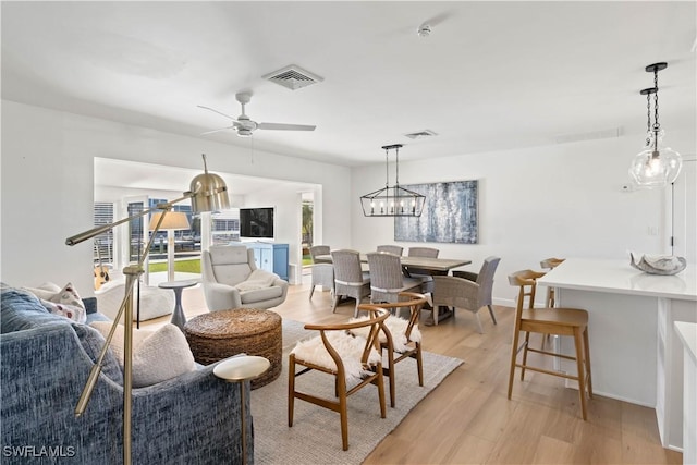 living room featuring visible vents, ceiling fan with notable chandelier, baseboards, and light wood finished floors