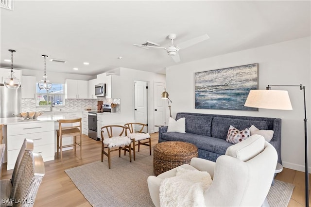 living room featuring visible vents, ceiling fan with notable chandelier, and light wood-type flooring