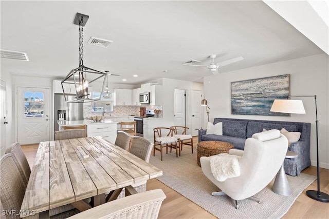 dining space with ceiling fan with notable chandelier, visible vents, and light wood finished floors