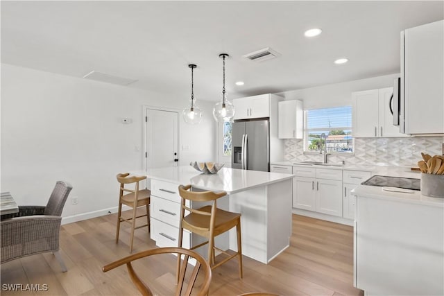 kitchen featuring a kitchen bar, visible vents, light wood-style flooring, a sink, and stainless steel fridge