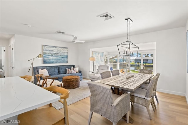 dining space with visible vents, light wood-style flooring, ceiling fan with notable chandelier, and baseboards