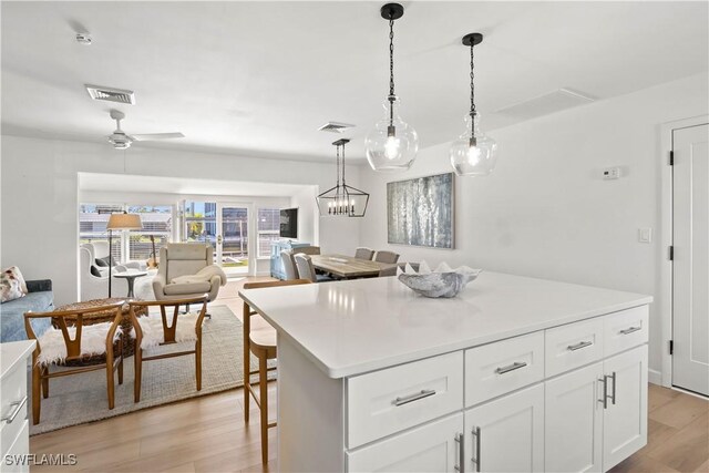 kitchen with light wood finished floors, visible vents, decorative light fixtures, open floor plan, and white cabinetry