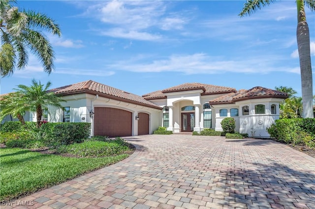 mediterranean / spanish home featuring a garage, a tile roof, driveway, french doors, and stucco siding