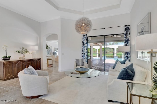 living room featuring a tray ceiling, baseboards, arched walkways, and a high ceiling