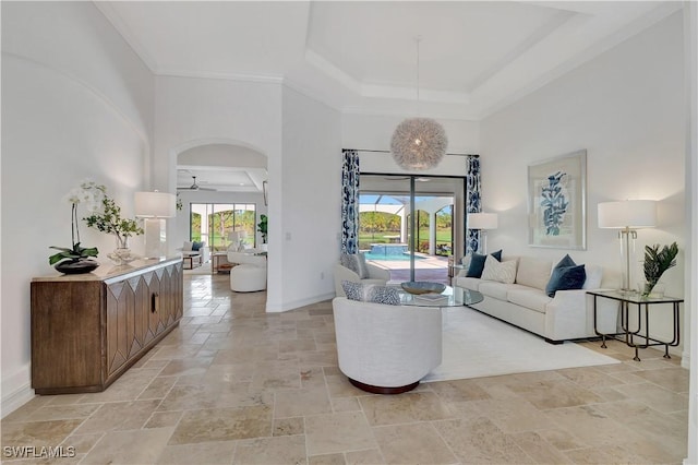 living area featuring stone tile flooring, a raised ceiling, a high ceiling, ceiling fan, and baseboards