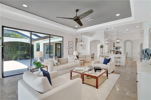 living area featuring a tray ceiling, visible vents, arched walkways, and recessed lighting