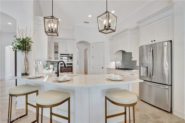 kitchen with arched walkways, appliances with stainless steel finishes, a peninsula, a sink, and a notable chandelier