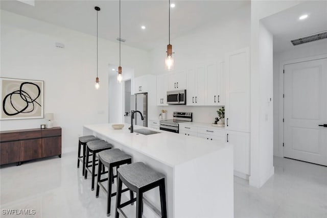 kitchen featuring visible vents, a kitchen bar, appliances with stainless steel finishes, white cabinetry, and a sink