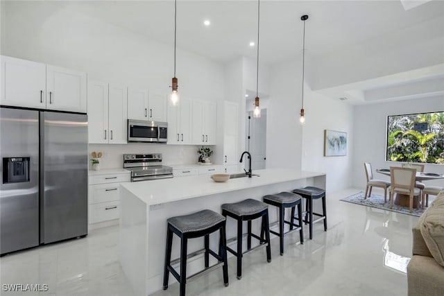 kitchen with appliances with stainless steel finishes, white cabinetry, a kitchen breakfast bar, and a sink