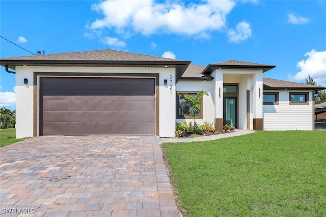 prairie-style house with stucco siding, decorative driveway, roof with shingles, an attached garage, and a front yard