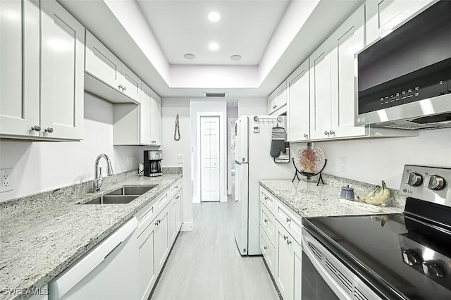 kitchen with a sink, light stone counters, white cabinetry, appliances with stainless steel finishes, and a raised ceiling