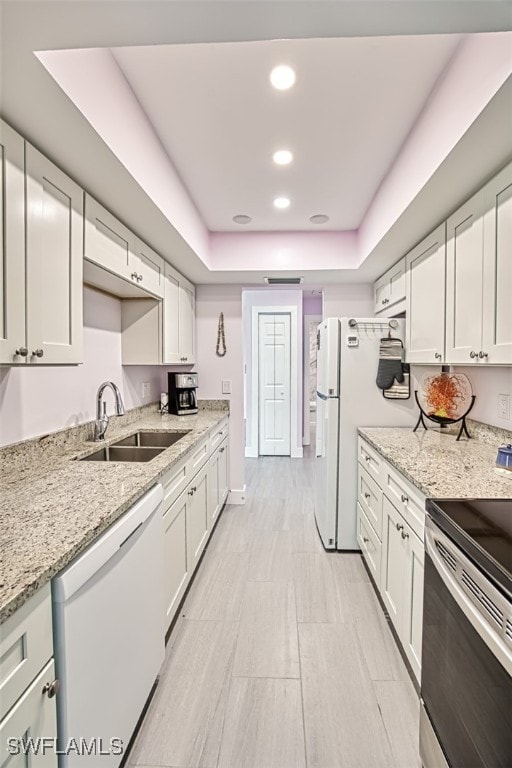 kitchen featuring a tray ceiling, recessed lighting, white appliances, white cabinetry, and a sink