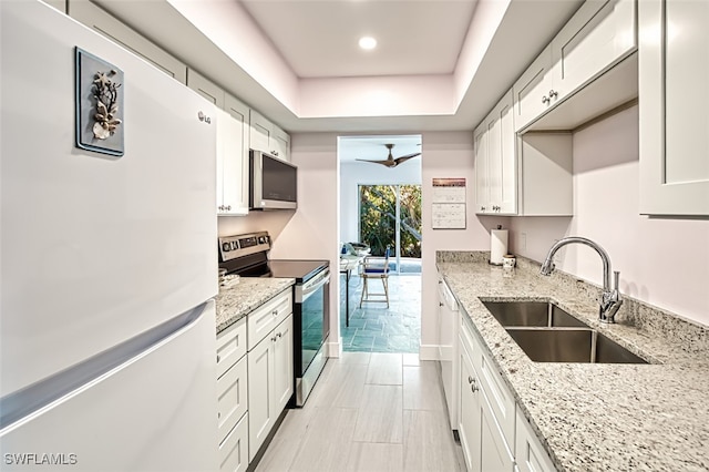 kitchen with a sink, light stone counters, white cabinetry, stainless steel appliances, and a raised ceiling