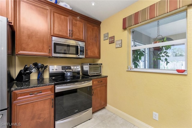 kitchen featuring light tile patterned flooring, a toaster, stainless steel appliances, baseboards, and dark stone countertops