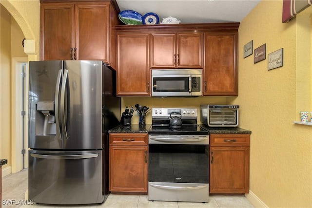 kitchen with light tile patterned floors, baseboards, dark stone counters, arched walkways, and appliances with stainless steel finishes