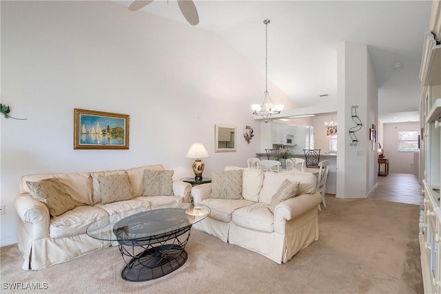 living room with ceiling fan with notable chandelier, light colored carpet, and high vaulted ceiling