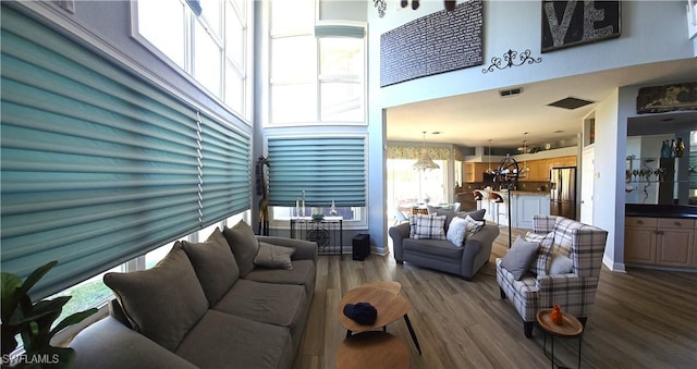 living area with a chandelier, dark wood-style flooring, a towering ceiling, visible vents, and baseboards