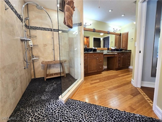 bathroom with baseboards, a tile shower, wood finished floors, and vanity