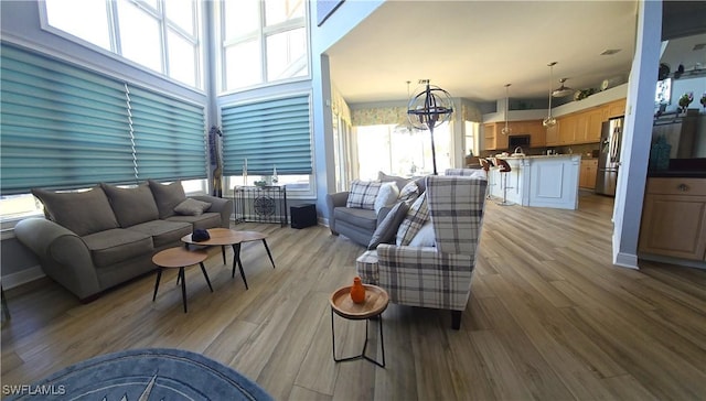 living area with a chandelier, a towering ceiling, light wood-style flooring, and baseboards