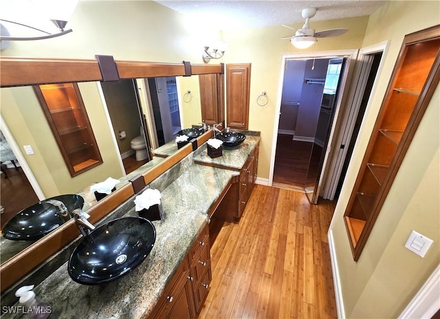 bathroom with a ceiling fan, toilet, wood finished floors, a spacious closet, and vanity