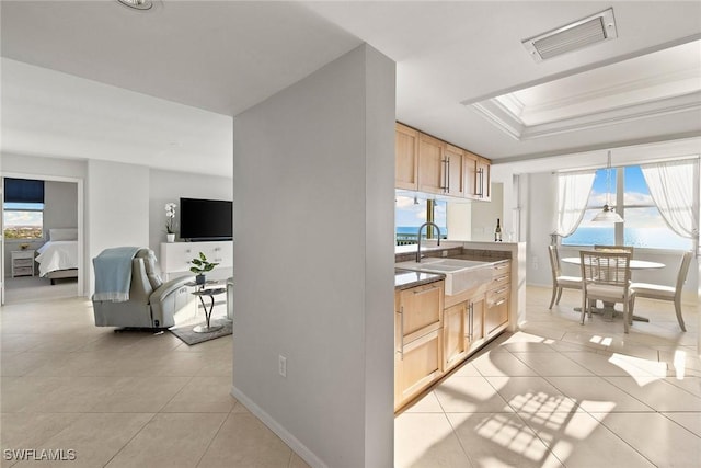 kitchen featuring visible vents, light brown cabinets, a sink, a tray ceiling, and light tile patterned floors