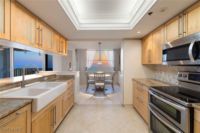 kitchen featuring a raised ceiling, ornamental molding, appliances with stainless steel finishes, and a sink