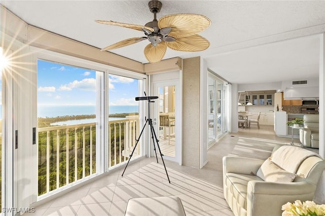 sunroom with a ceiling fan, visible vents, a healthy amount of sunlight, and a water view