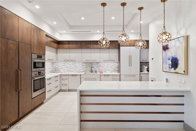 kitchen with white built in refrigerator, a sink, light countertops, decorative light fixtures, and backsplash