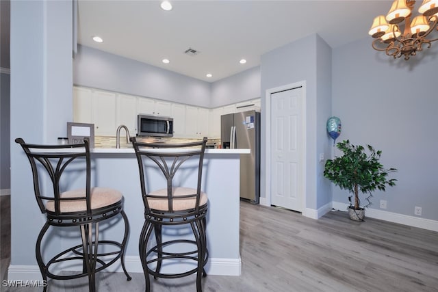 kitchen with visible vents, appliances with stainless steel finishes, white cabinets, light wood-type flooring, and a peninsula