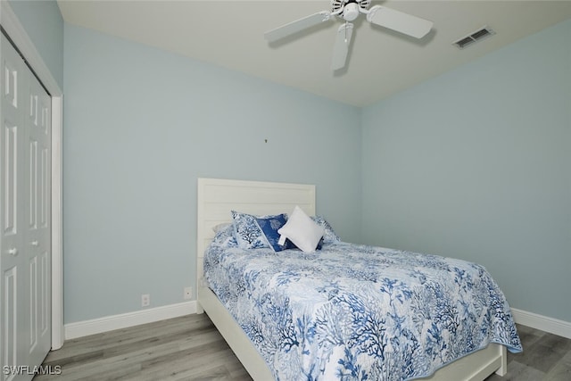 bedroom with ceiling fan, wood finished floors, visible vents, baseboards, and a closet