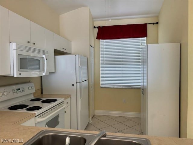 kitchen with light tile patterned floors, light countertops, white cabinets, white appliances, and baseboards